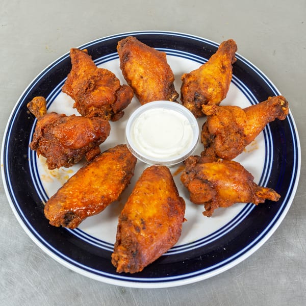 A plate of eight crispy, golden-brown chicken wings with a side of ranch dressing.