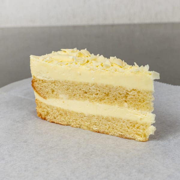 A slice of Mama Ginna's Italian vanilla cake with creamy frosting and white chocolate shavings.