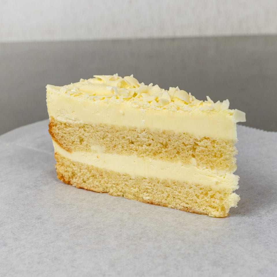 A slice of Mama Ginna's Italian vanilla cake with creamy frosting and white chocolate shavings.