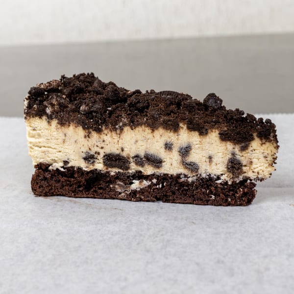 A slice of cookies and cream cheesecake with a chocolate cookie crust and crumbled topping.