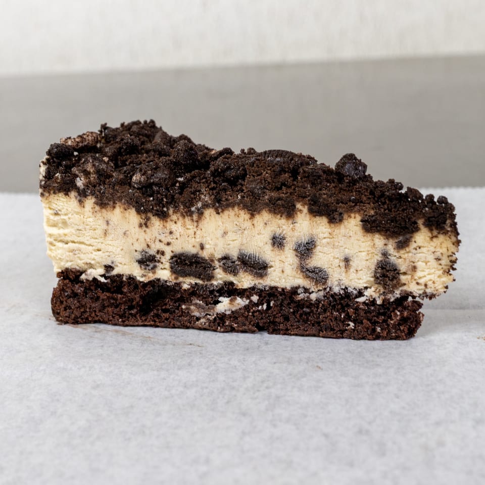 A slice of cookies and cream cheesecake with a chocolate cookie crust and crumbled topping.