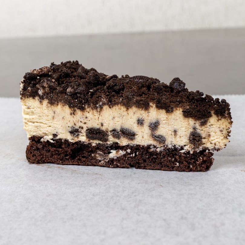 A slice of cookies and cream cheesecake with a chocolate cookie crust and crumbled topping.